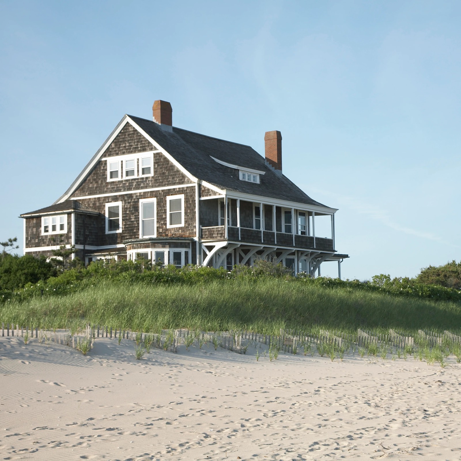 A weathered shingle-style beach house standing alone above the dunes, watched over out of season.