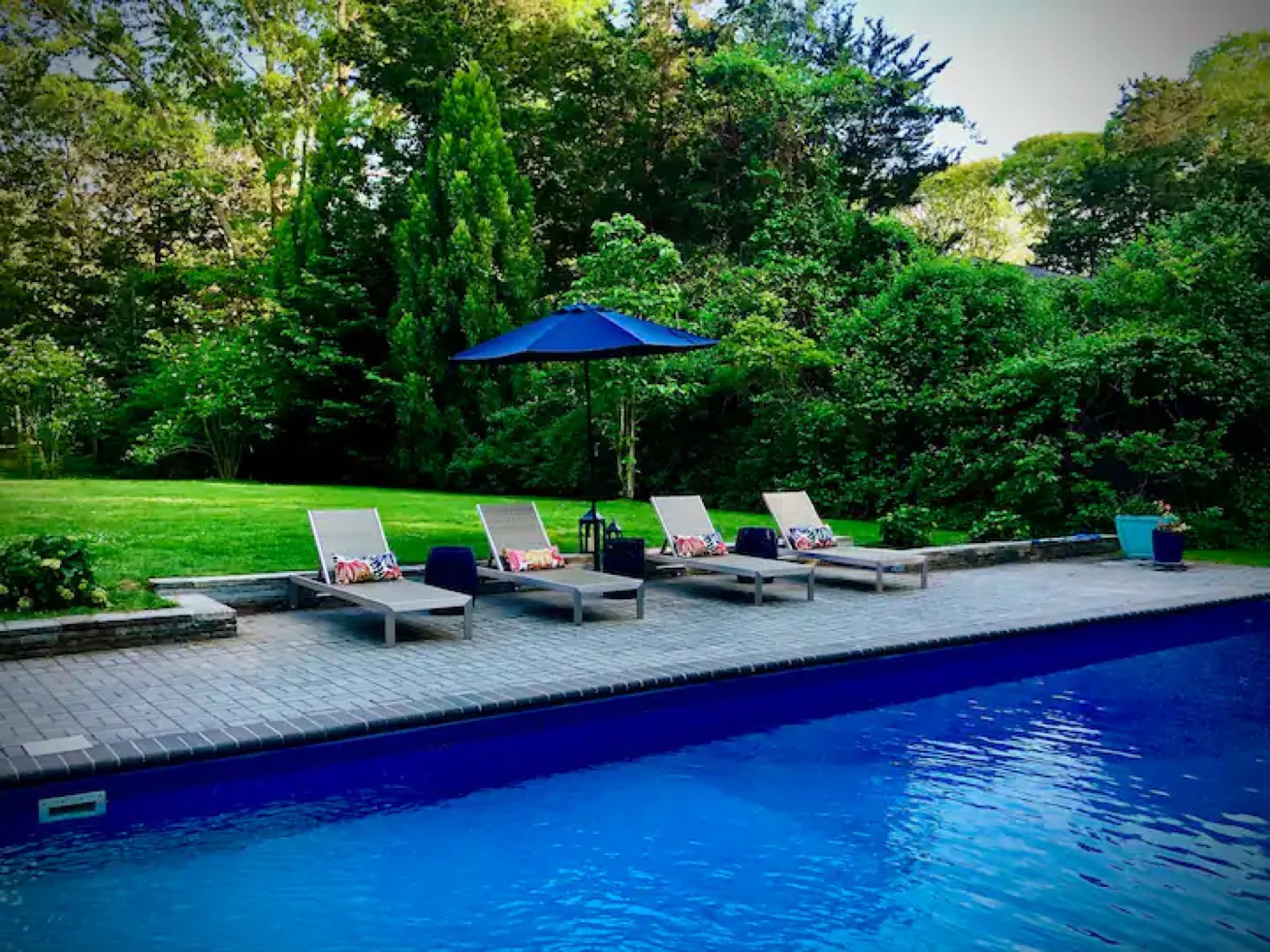A backyard pool and loungers opened and readied for the season under blue umbrellas.